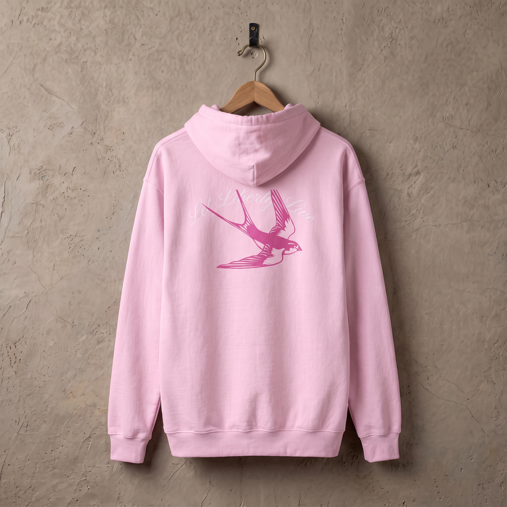 Let Liberty Live hoodie in lichtroze aan een houten hanger tegen een stucwerk muur